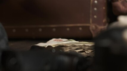 Old money is put on table next to black gun and brown leather suitcase. 1920s concept in vintage style, gangsters, mafia.