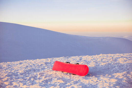 A red snowboard on a snowy slope at sunset