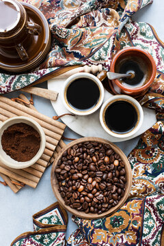 Overhead view of a bowl of coffee beans, next to ground coffee, a cup of coffee and a patterned scarf.