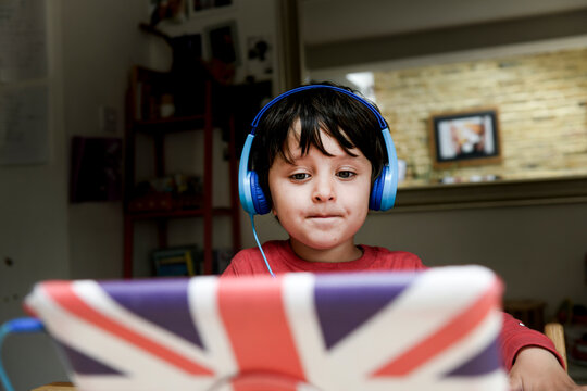 A five year old boy in blue headphones having an interactive learning session, home schooling. 