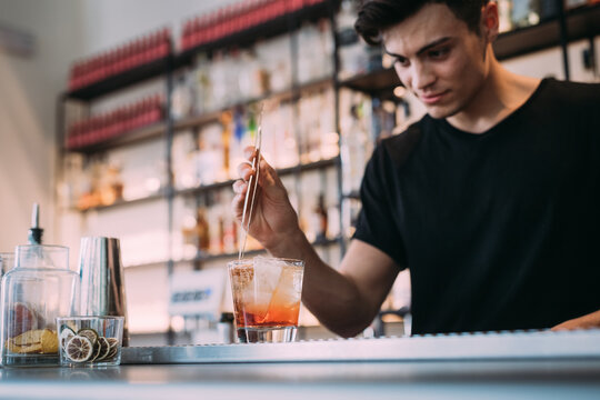 Young man wearing black clothes standing behind bar counter, preparing drink.