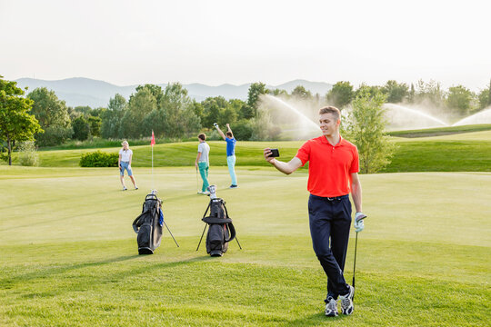 Man taking selfie on golf course, friends playing golf in background 