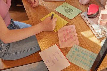 Teenage girl sitting in her room at a desk, writing motivational quotes on note cards.