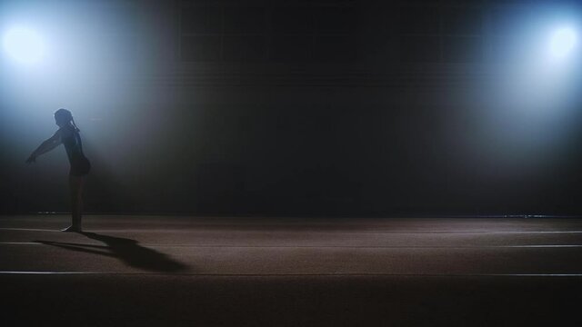 backflip of teen girl gymnast on spring floor in sports hall, slow motion shot, side view, training of talented sporty child