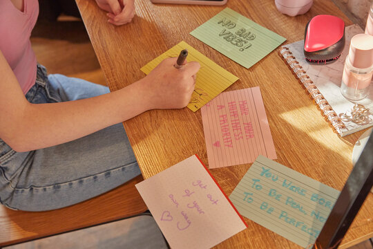 Teenage girl sitting in her room at a desk, writing motivational quotes on note cards.