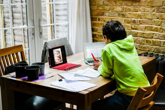 A boy sitting at a desk using a laptop for an interactive learning session, home schooling, working hard. 