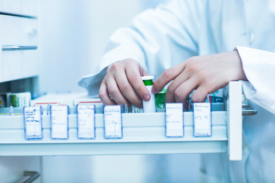 Close up of pharmacist standing next to a drawer with medicines in pharmacy.