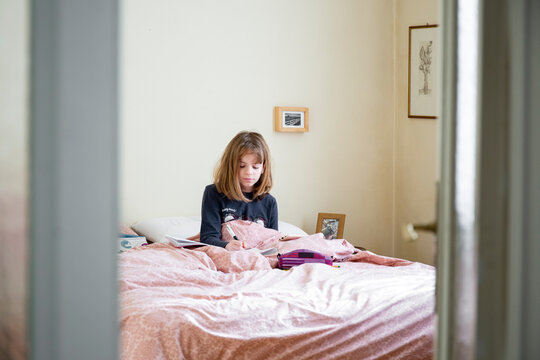 Girl sitting on her bed in her room, studying, home schooling with laptop and notebook