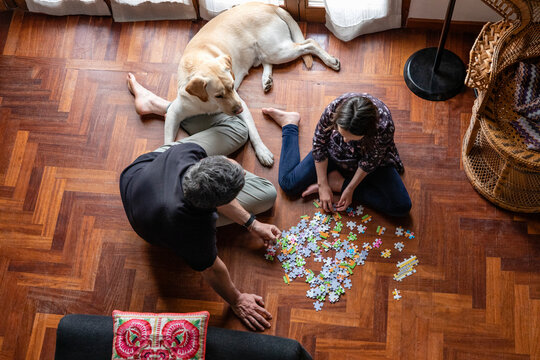 Father and daughter sitting on living room floor, doing jigsaw puzzle during Coronavirus lockdown.
