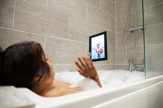 Woman sitting in bathtub, having foam bath and using digital tablet during Coronavirus crisis.