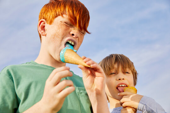 Two boys standing outdoors, eating ice cream cones. 