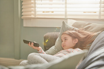 Girl lying on a sofa in her pajamas, watching television.