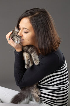 Studio shot of woman hugging grey cat, on grey background.