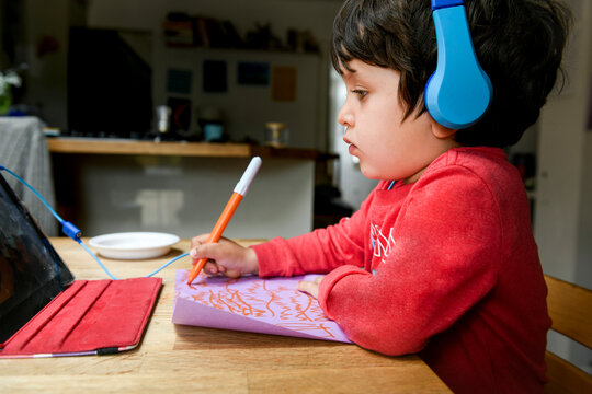 A five year old boy in blue headphones having an interactive learning session, home schooling. 