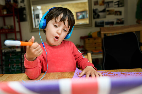 A five year old boy in blue headphones having an interactive learning session, home schooling. 