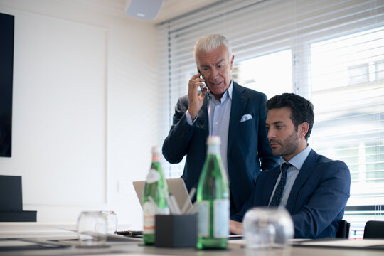 Two businessmen in an office, typing on laptop and using mobile phone.