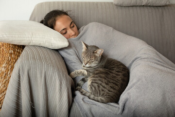 Woman and grey tabby cat sleeping on a sofa.