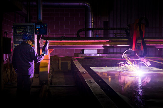 Man working in a steel factory, operating computerized welding machine.