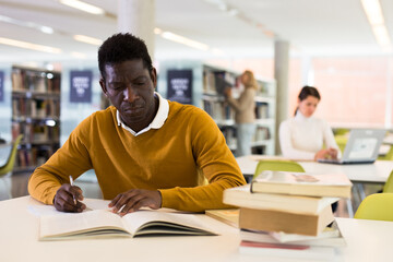 Intelligent african-american male student engaged in research working with books in university library. High quality photo