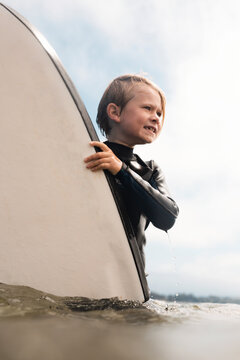 Portrait of young boy wearing wet suit, carrying surfboard into ocean, Santa Barbara, California, USA.