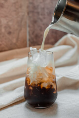 Barista pouring milk into a glass of iced coffee