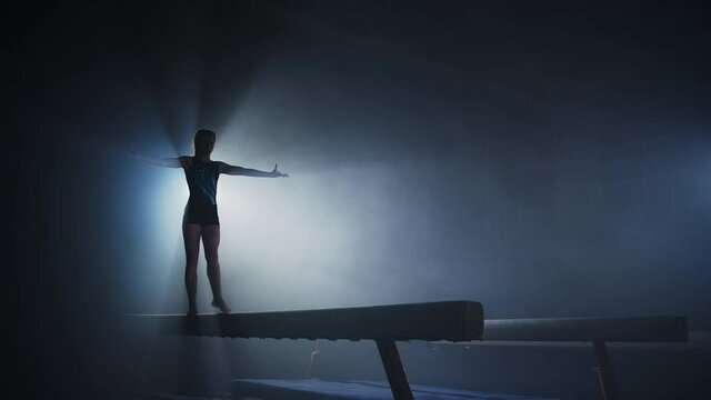 competition of artistic gymnastics in children sport school, teen girl is performing on balance beam, silhouette