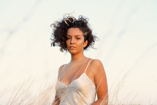 Portrait of beautiful woman with brown curly hair hair, wearing white silk chemise.