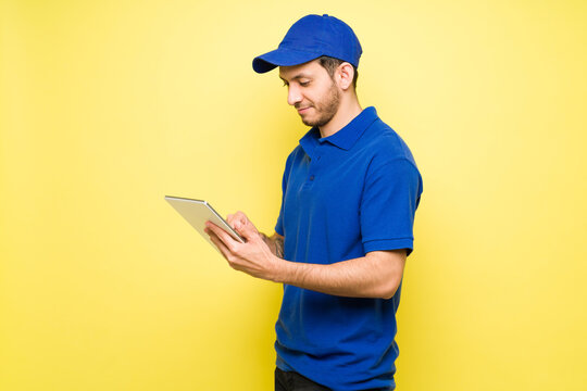 Latin Delivery Man With A Cap Using A Tablet