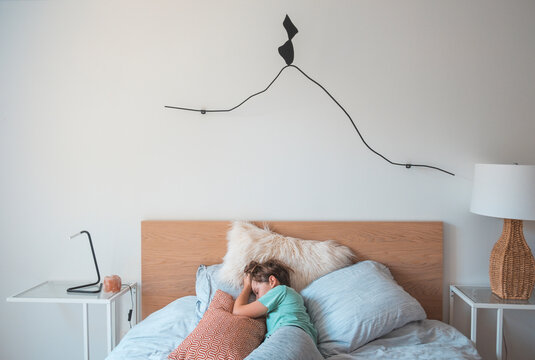 Boy lying in  double bed with wooden headboard, taking a nap.