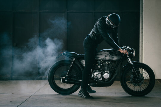 Young Male Motorcyclist Revving Vintage Motorcycle In Garage