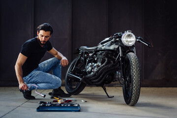 Young male motorcyclist doing maintenance on vintage motorcycle in garage