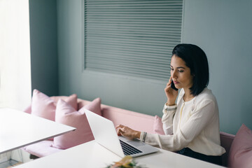 Young businesswoman at hotel table looking laptop and using smartphone
