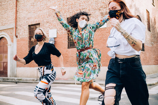Three young women wearing face masks during Corona virus, running across a pedestrian crossing in a street.