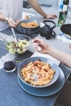 High angle close up of two people standing at a table, eating bowls of Fusili pasta.