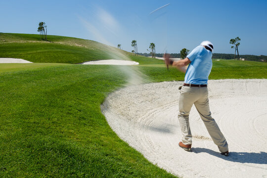 Male golfer chipping out of sand trap. 