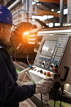 Man working in a steel factory, operating computerized machine.