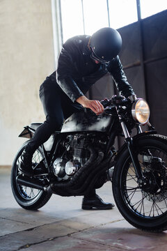 Young male motorcyclist revving vintage motorcycle in garage