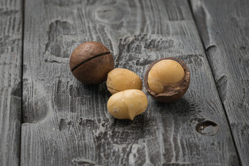 One whole and three peeled macadamia nuts on a wooden table.