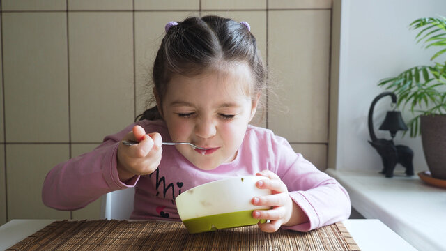 Adorable little girl enjoys eating vegetable soup with good appetite.