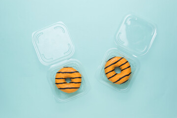 Two doughnuts in open plastic delivery boxes on a blue background.