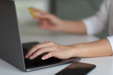 Close up hand of woman using laptop computer and credit card for shopping online at home.
