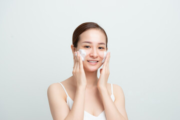 Image of adorable asian woman washing her face with foaming facial cleanser isolated over white background