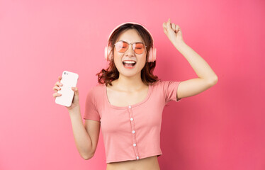 Young asian girl wearing headphones and using the phone on pink background