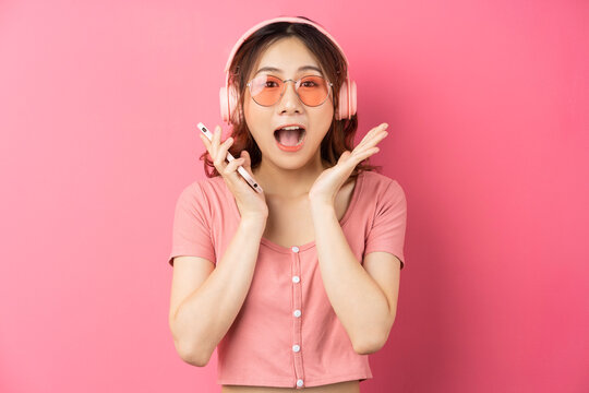Young asian girl wearing headphones and using the phone on pink background