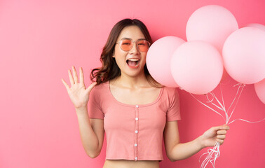 The beautiful lady wears glasses and holds balloons on a pink background