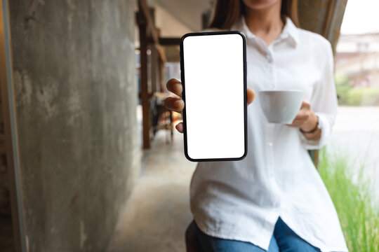 Mockup image of a beautiful woman showing a mobile phone with blank white screen while drinking coffee