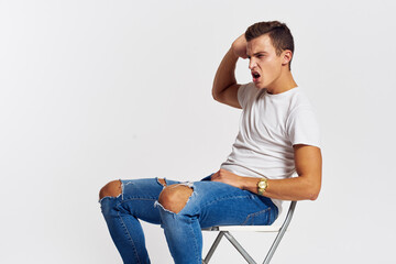 Man on a chair indoors torn jeans white t-shirt handsome face model light background