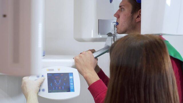 Modern dental X-Ray scanner makes a panoramic radiograph of the jaw of young man. Nurse controls the process