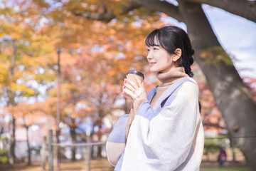 Fototapeta premium 秋の公園でコーヒーを飲む女性（笑顔） 