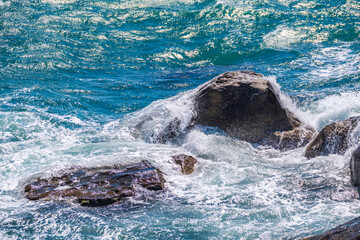 Sea waves of dark water beat against the coastal rocks. An infinite number of splashes, drops of water and white foam are scattered.